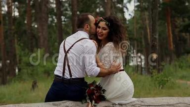 <strong>奢华</strong>幸福的新娘和时尚的新郎，坐在夏日森林的原木上..